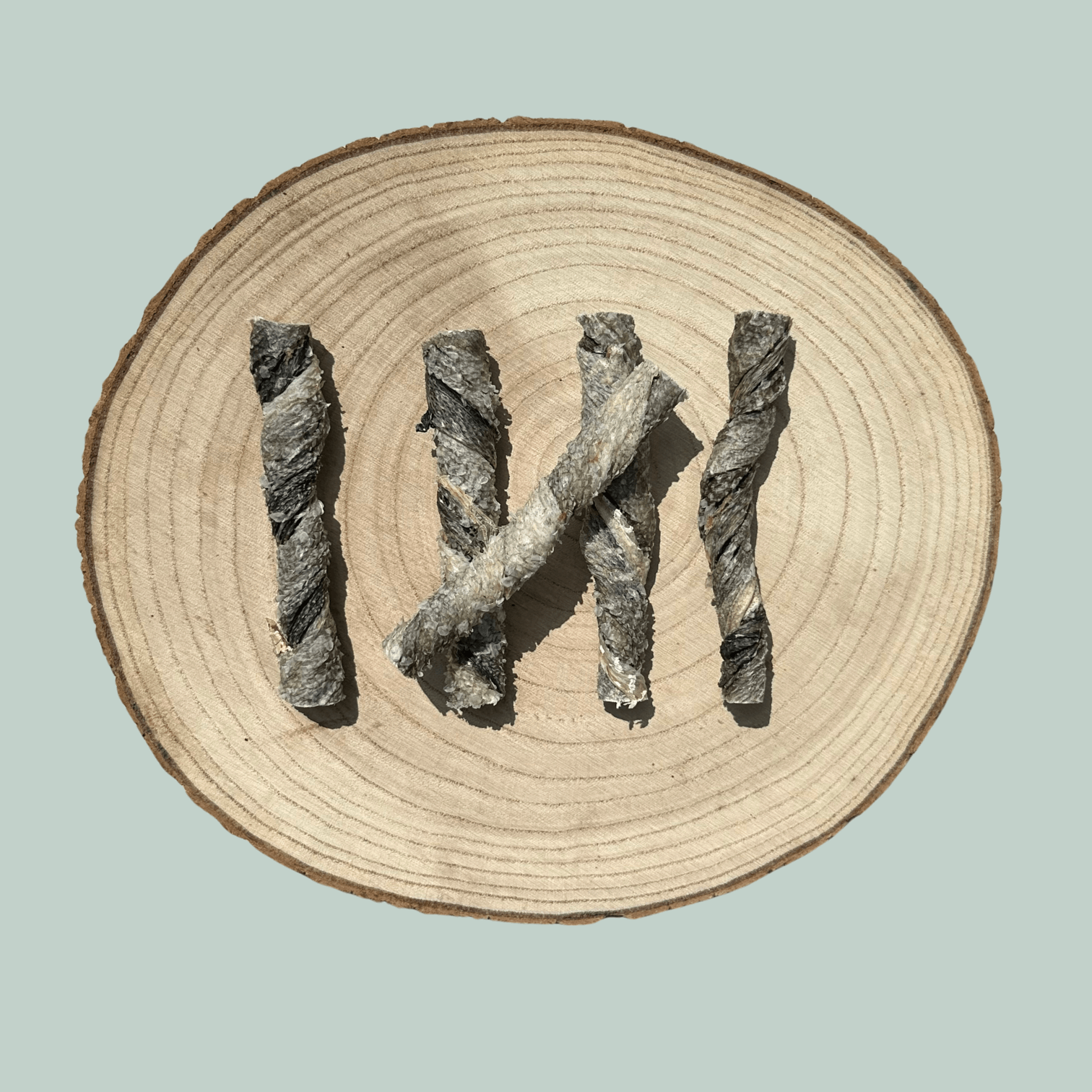 5 dried salmon skin dog treats on a natural wooden slice plate against a jade green background