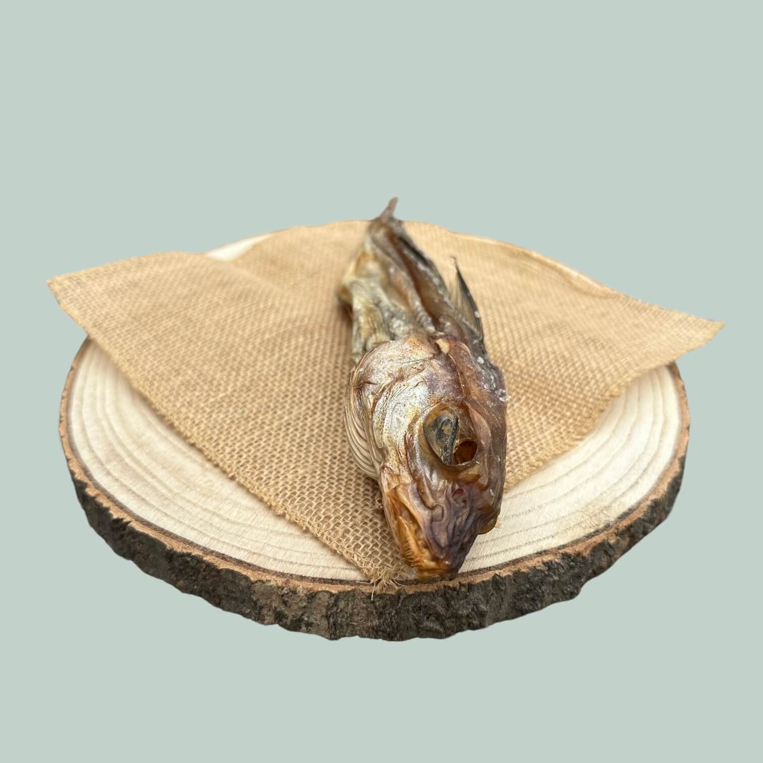 Side view of a whole dried haddock fish chew on a wooden plate