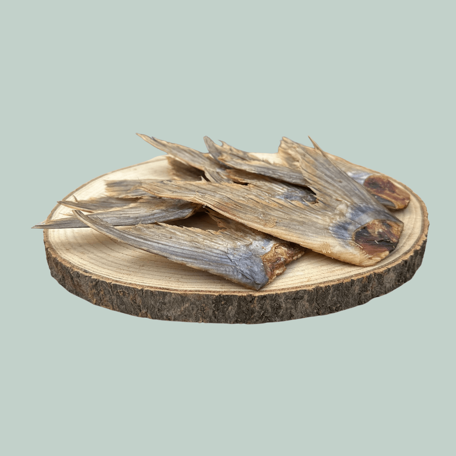 Side view of a pile of dried catfish tail natural and healthy dog treats on a wooden slice plate against a jade green background