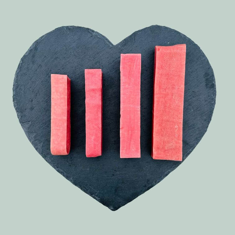 Full range of strawberry yak bars for dogs on a slate plate and jade green background