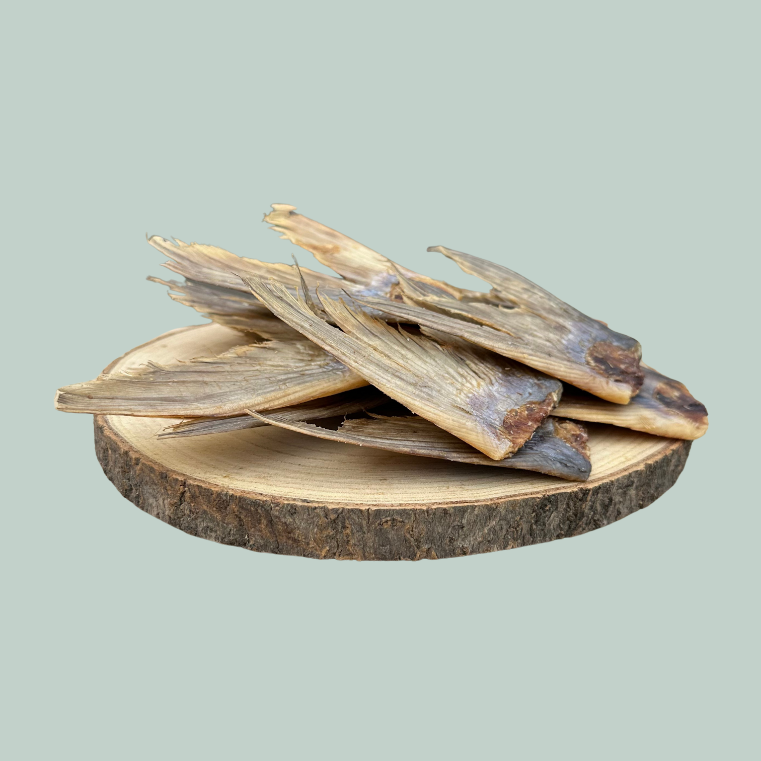 Side view of a pile of dried catfish tail natural and healthy dog treats on a wooden slice plate against a jade green background