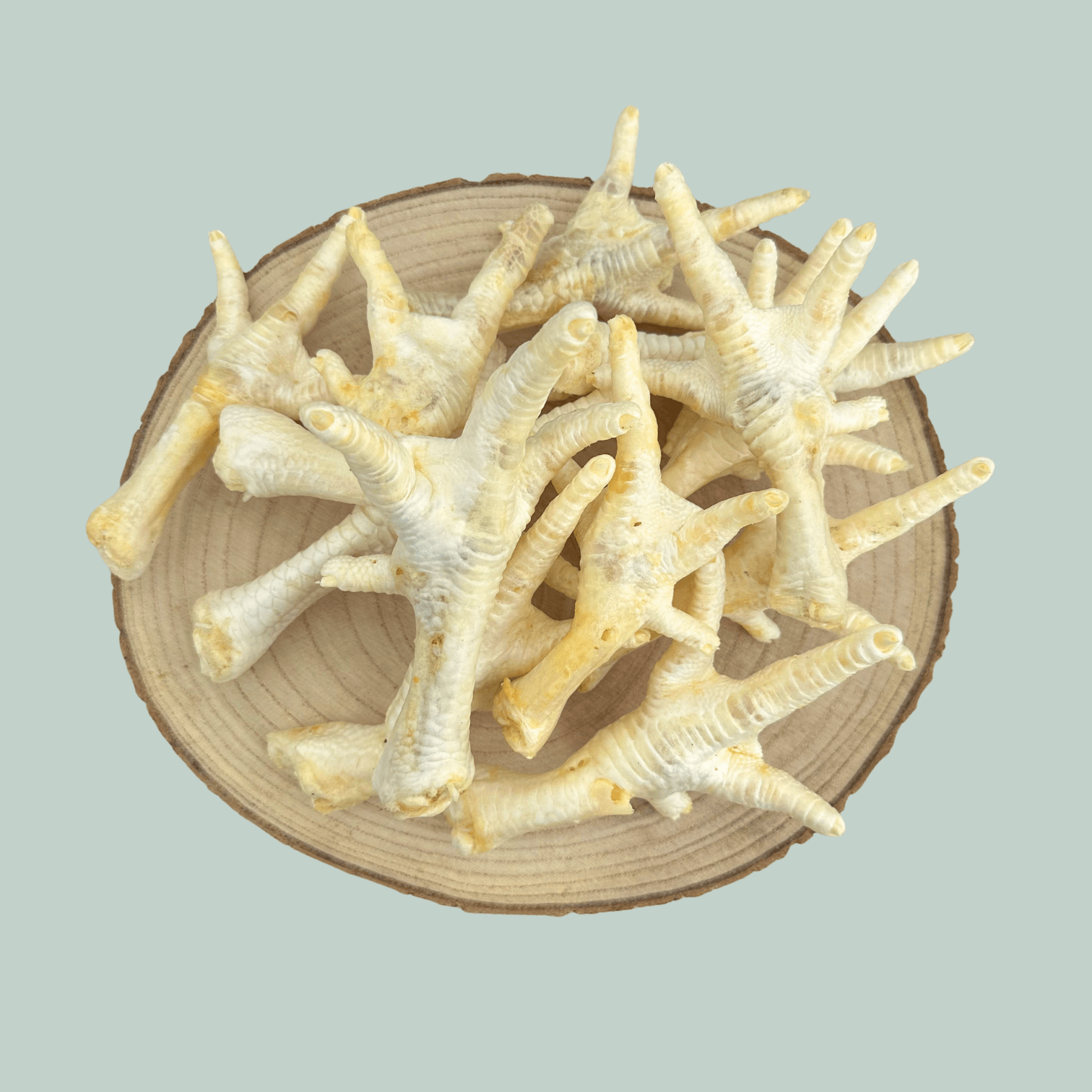 Pile of dried and puffed chicken feet for dogs and puppies on a wooden slice plate against a jade green background