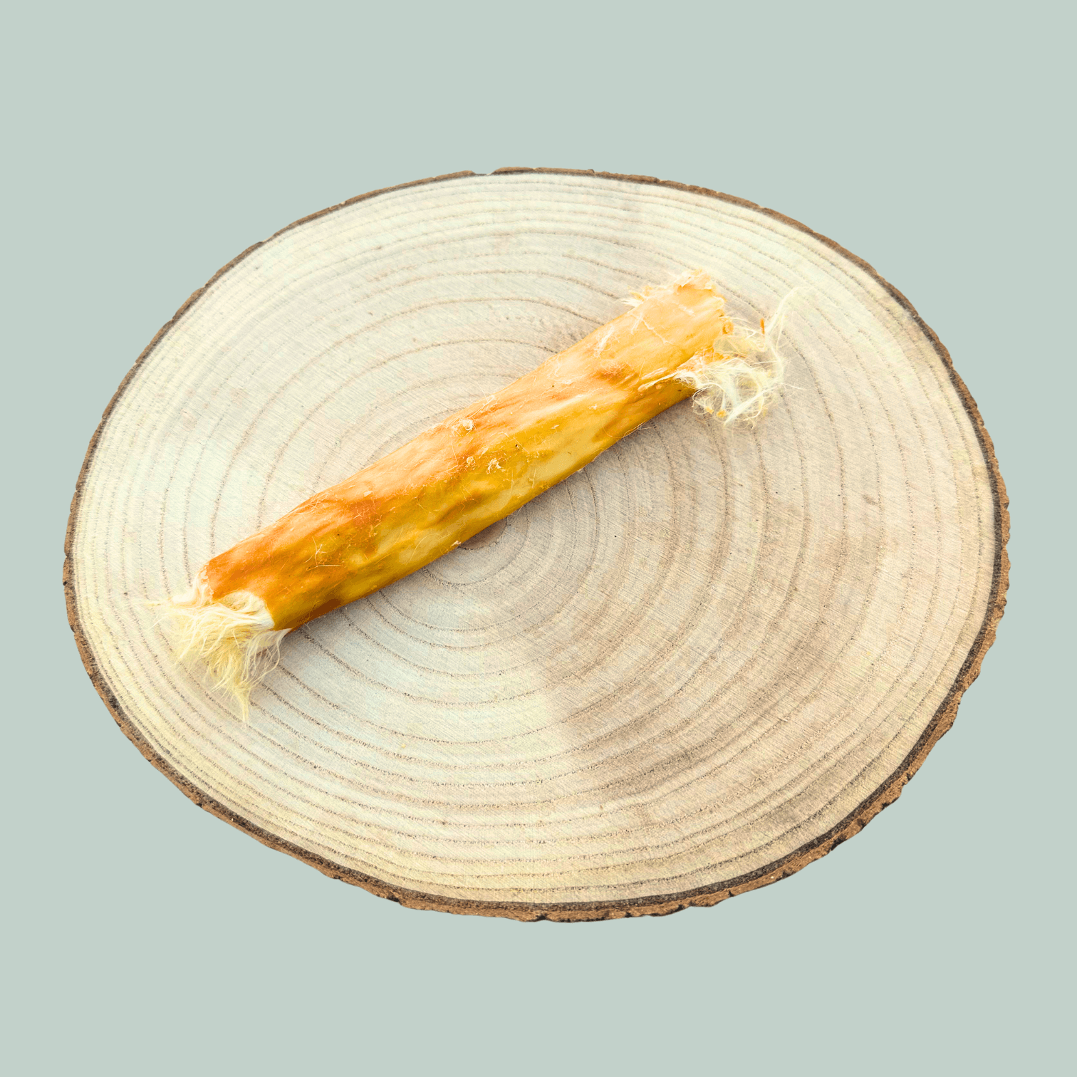 Single rabbit skin roll natural dog chew on a wooden slice plate against a jade green background.