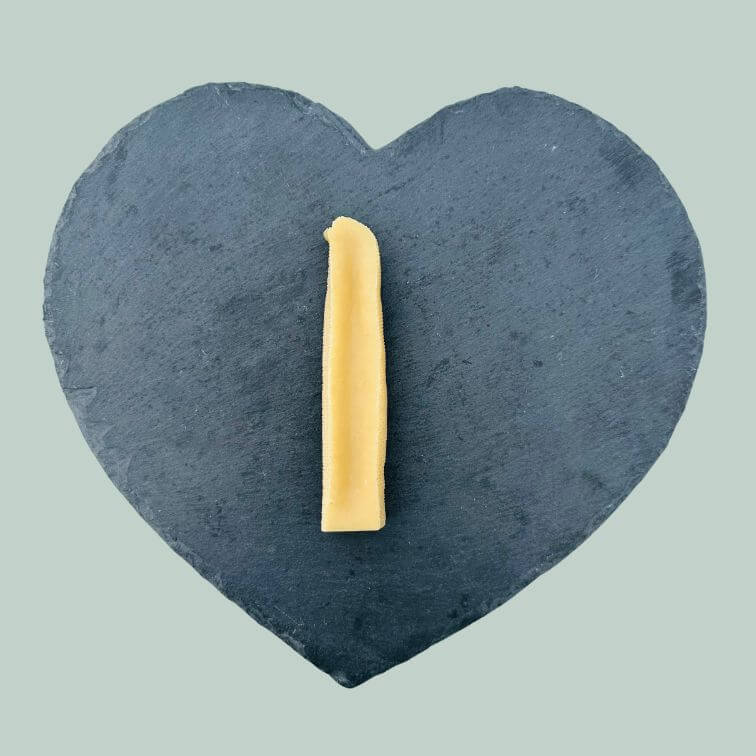 Single medium yak cheese bar for dogs on a slate plate and jade green background