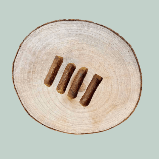 4 single protein venison sausages for dogs on a wooden slice plate against a jade green background.