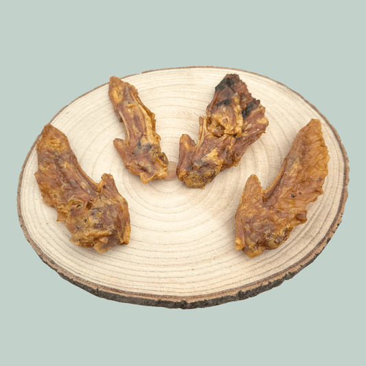 4 dried turkey wing dog chews on a wooden slice plate against a jade green background.