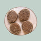 4 premium quarter pounder beef burgers for dogs on a wooden plate and jade green background