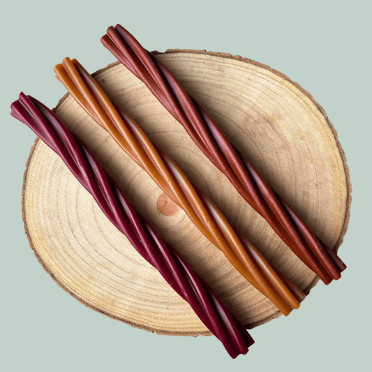 Three chewy dog treats in red, brown, and orange on a wooden surface with a light gray background
