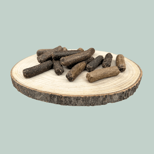 A pile of all natural pure venison sausages for dogs on a wooden slice plate against a jade green background.