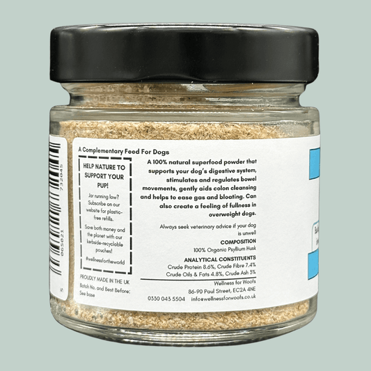 A glass jar with a black lid containing Organic Psyllium Husks for dogs. The label explains that they are a natural superfood that supports the dog's digestive system, stimulates and regulates their bowel movements and gently aids colon cleansing, helping to relieve gas and bloating.