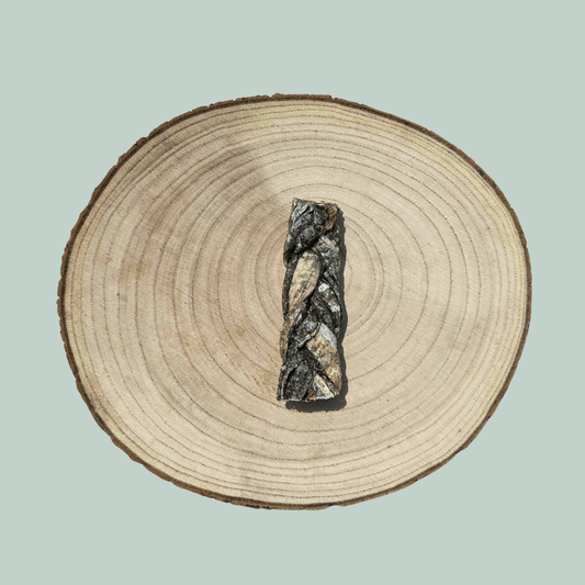 Single natural cod skin braid dog chew on a wooden slice plate against a jade green background