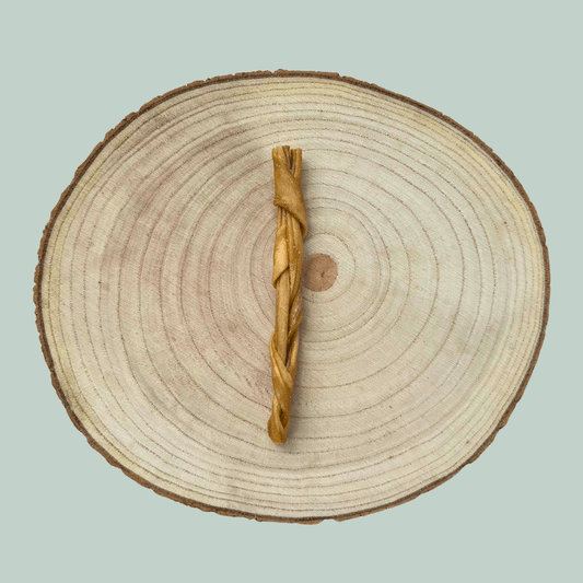 Single braided lamb skin chew for dogs on a wood slice plate against a jade green background