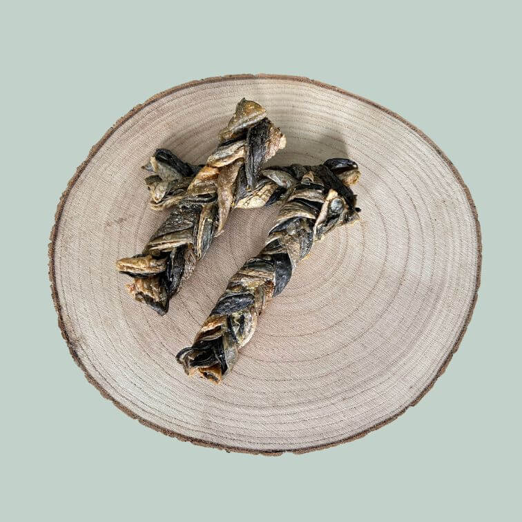 Braided dried salmon skin treat for dogs on a wooden slice plate and jade green background