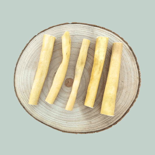 5 dried buffalo tail piece natural dog chews on a wooden slice plate against a jade green background.