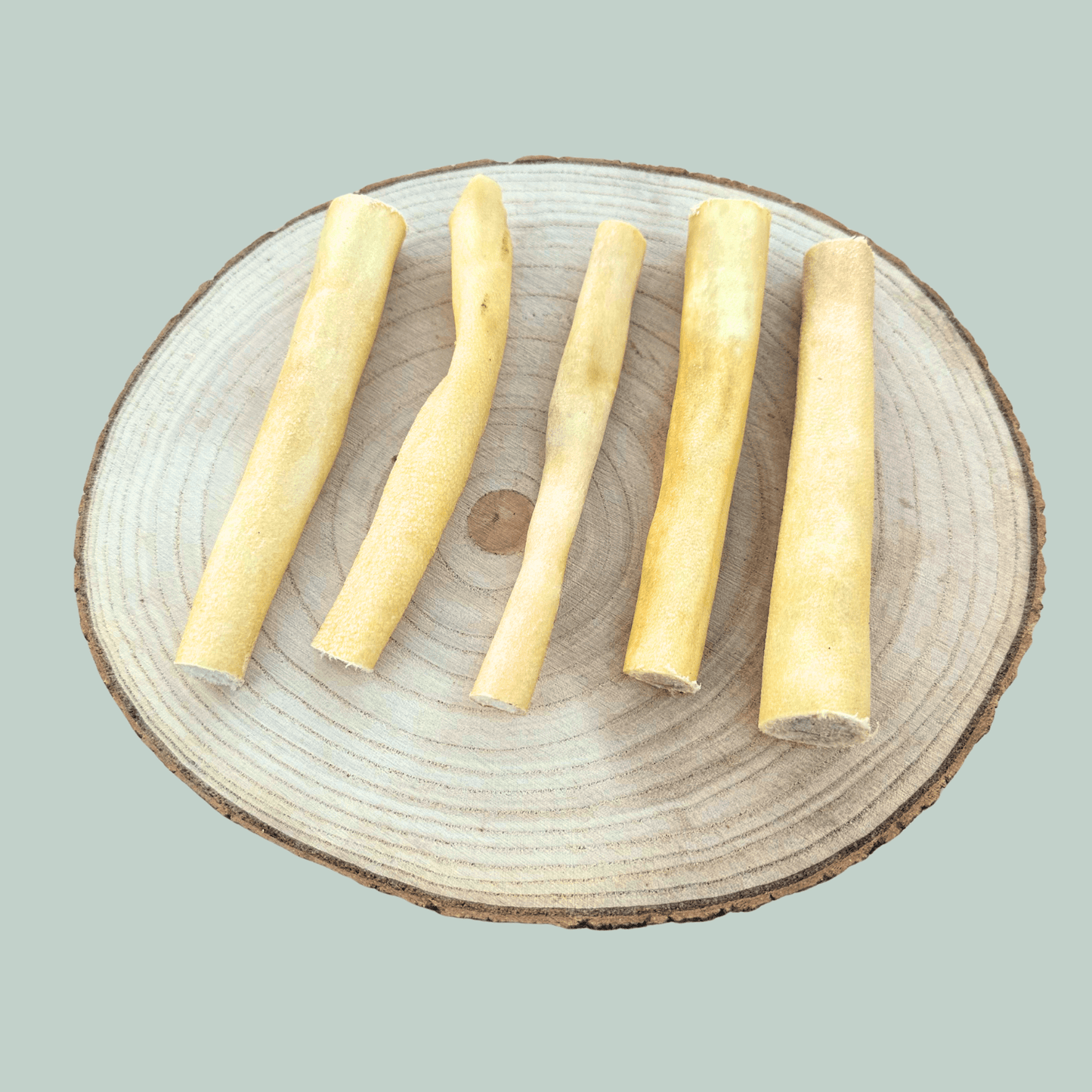 5 dried buffalo tail piece natural chews for dogs on a wooden slice plate against a jade green background.