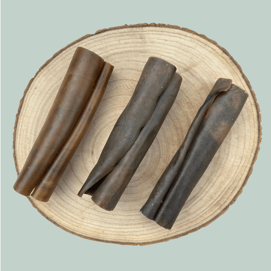 3 small rolls of dried camel skin natural and healthy long lasting dog chews on a wooden slice plate against a jade green background.