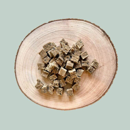 A pile of cod and mango cube dog treats on a wood slice plate and jade green background