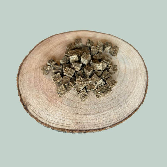 A pile of cod and mango cube dog treats on a wood slice plate and jade green background