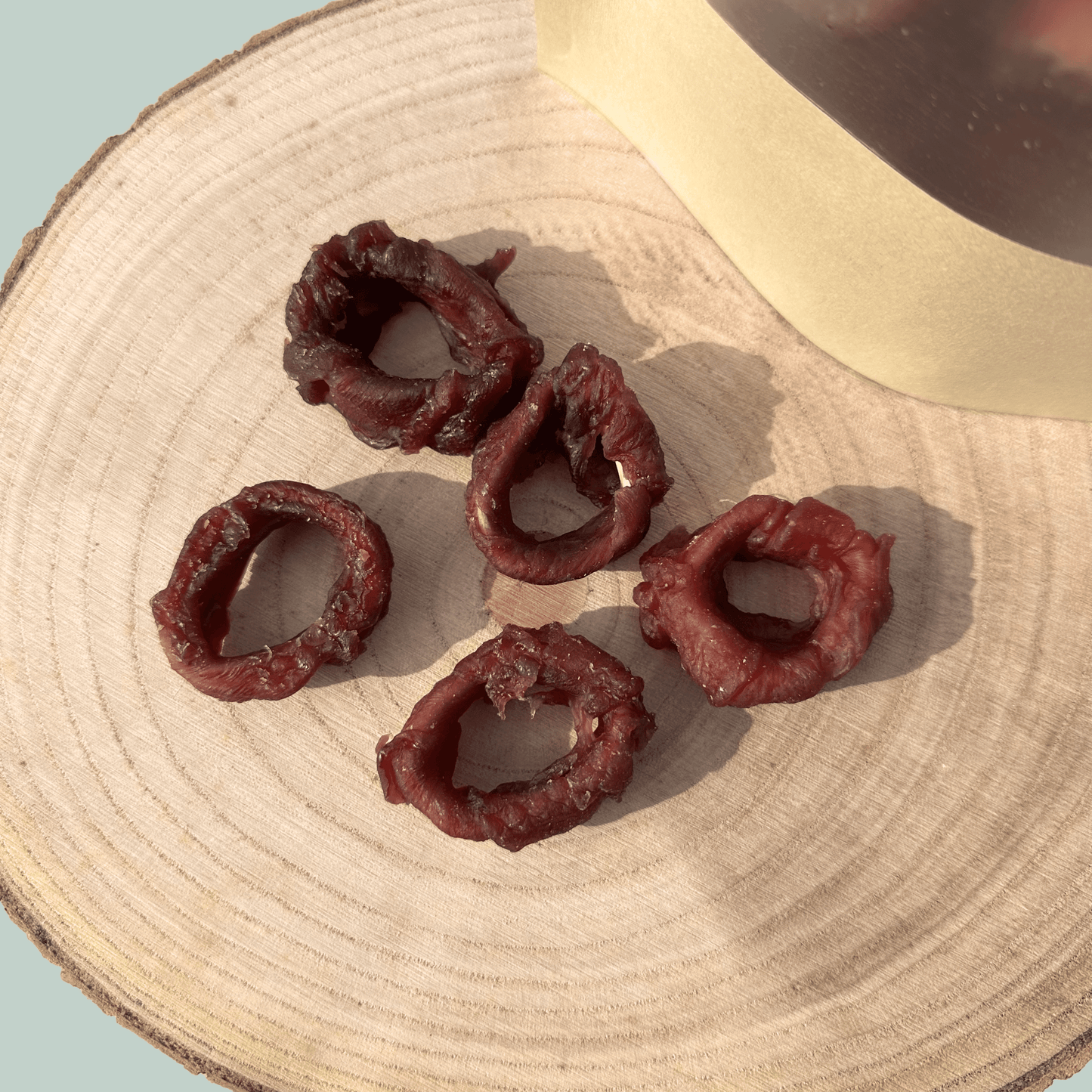 Five dried squid ring dog treats on a wooden surface with a light blue background