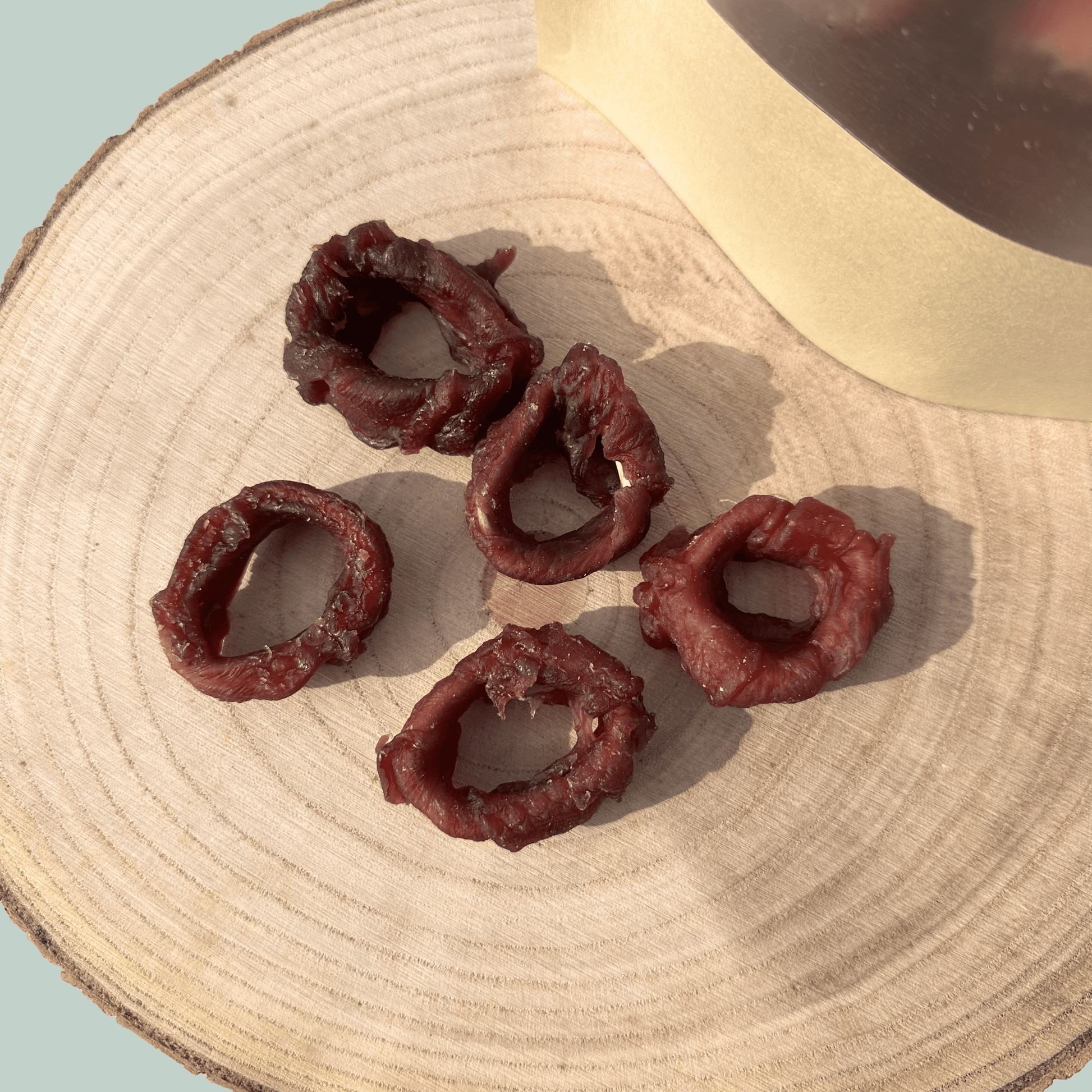 Five dried squid ring dog treats on a wooden surface with a light blue background