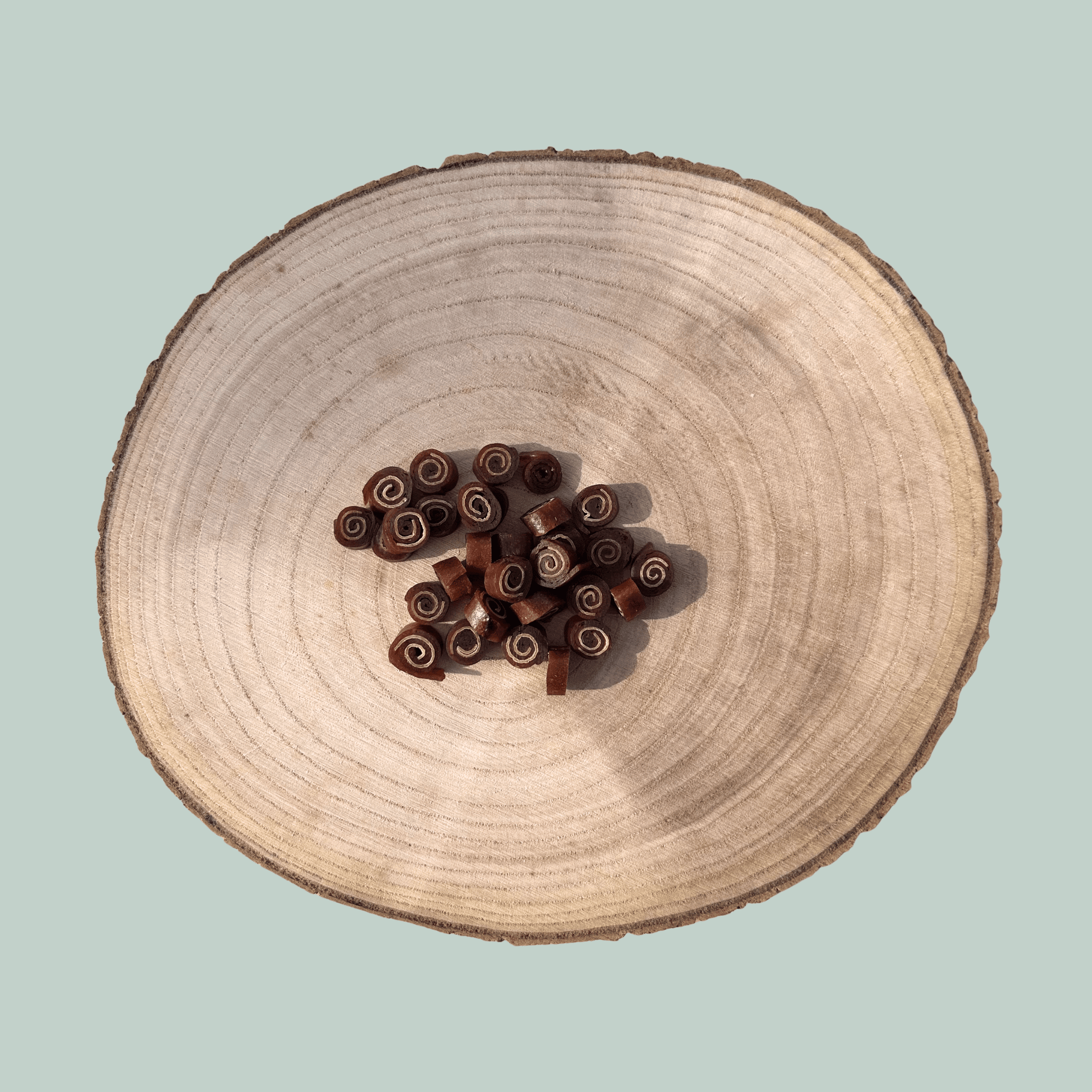 Pile of duck and cod training treats for dogs on a wooden plate.