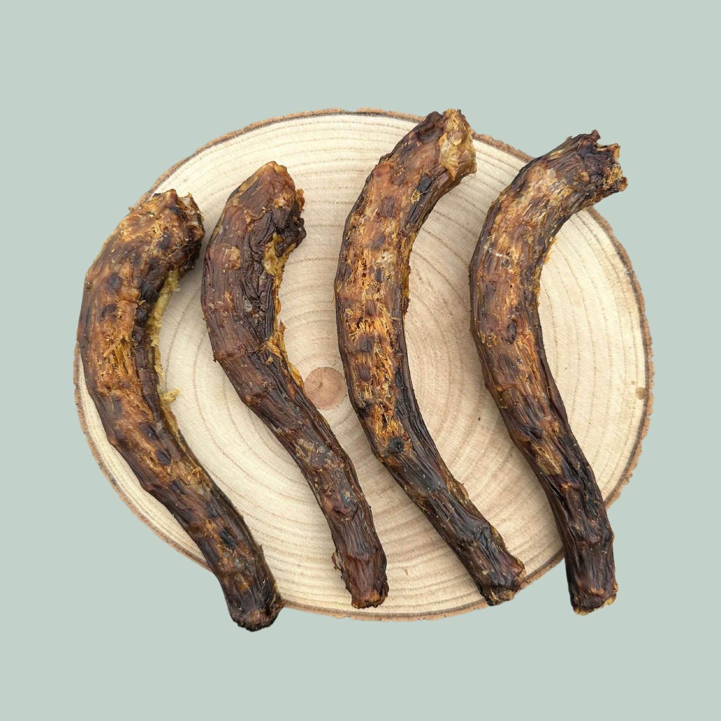 Four dried goose neck dog chews on a wooden slice plate and jade green background