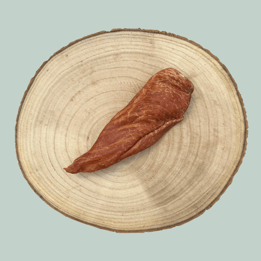 A single dried chicken fillet natural and healthy dog chews on a wooden slice plate against a jade green background