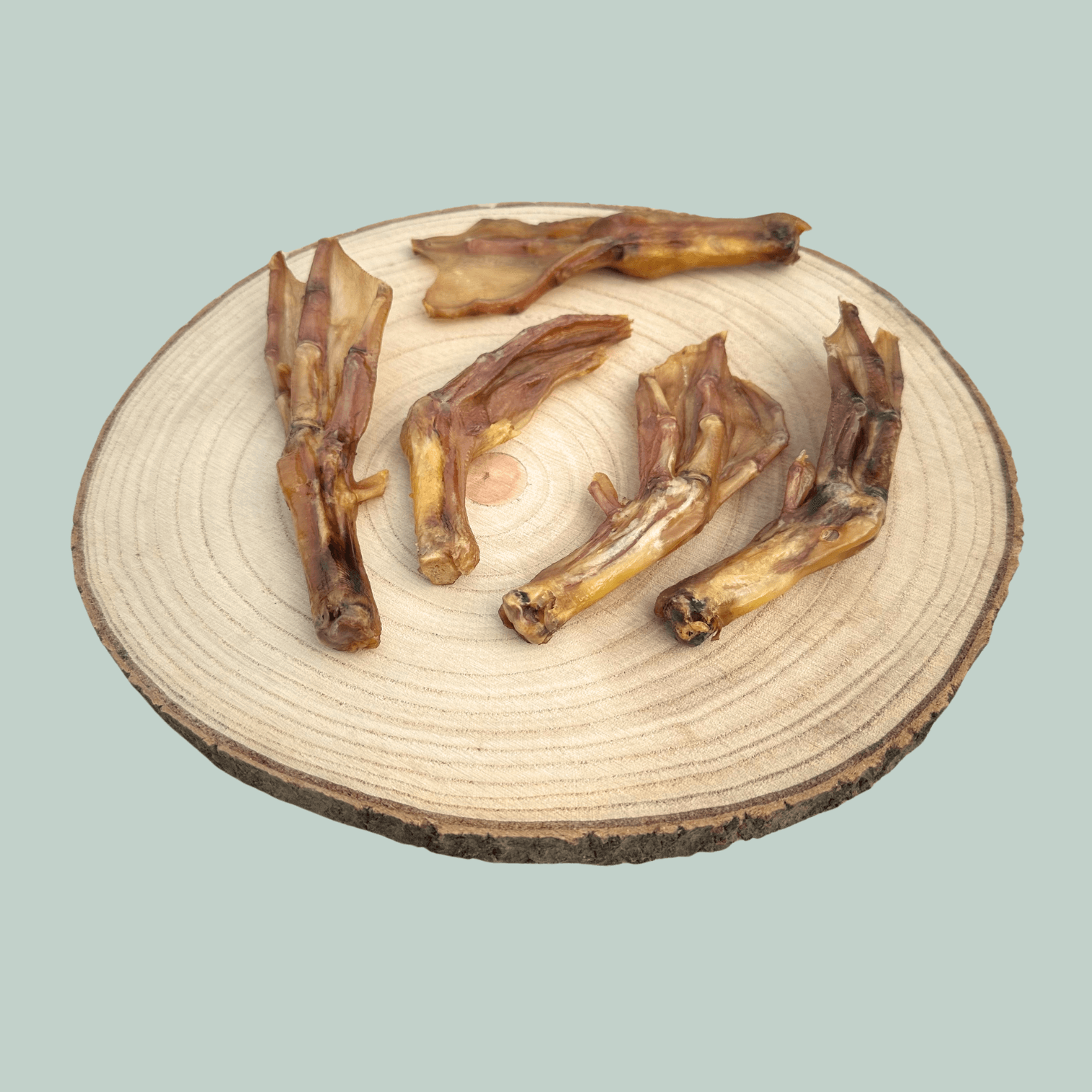Five dried duck feet dog treats on wooden plate in front of a green backdrop.