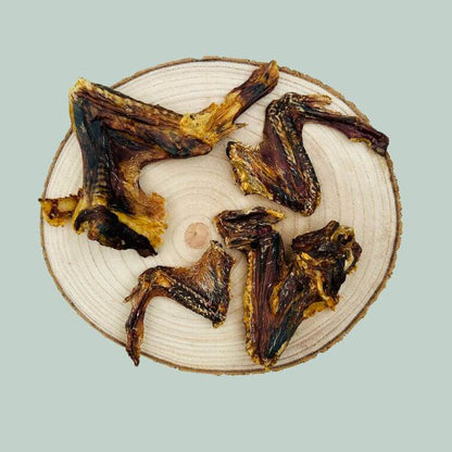 4 dried duck wing dog treats on a wooden slice plate and jade green background