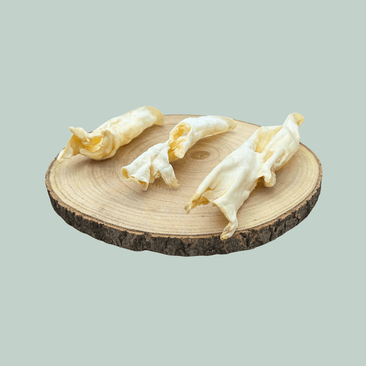 Side view of 3 dried lamb ear natural dog chews on a wooden slice plate against a jade green background