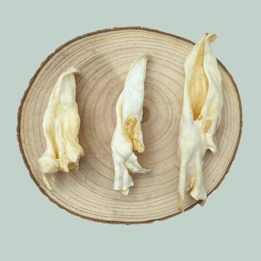 3 dried lamb ear natural dog chews on a wooden slice plate against a jade green background