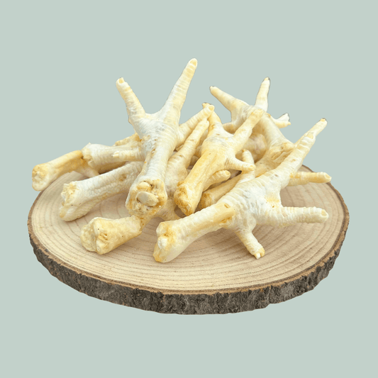 Side view of a pile of dried and puffed chicken feet for dogs and puppies on a wooden slice plate against a jade green background