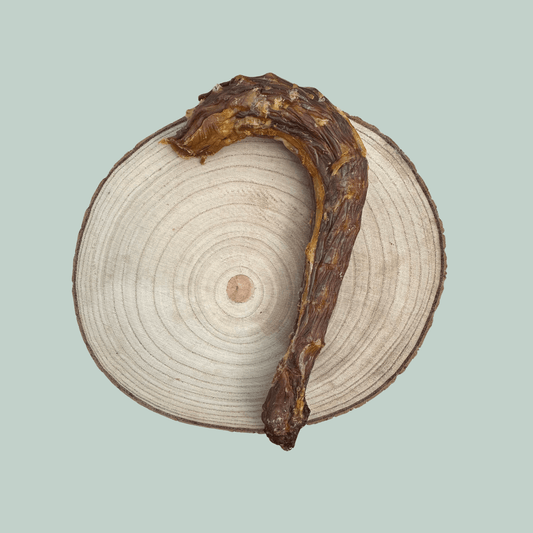 A dried turkey neck dog chew on a wooden plate against a green backdrop.