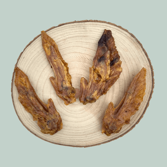 4 dried turkey wing dog chews on a wooden slice plate against a jade green background.