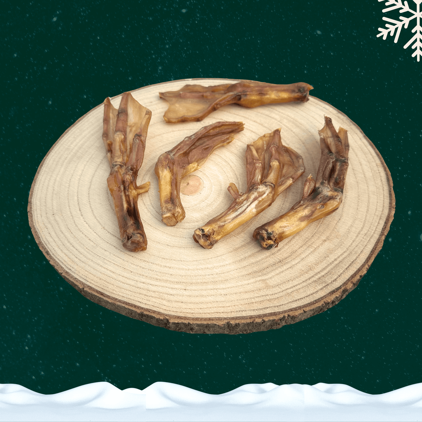 Five dried duck feet dog treats on wooden plate in front of a green starry sky backdrop with a white snowflake in the top right corner and a blanket of snow across the bottom.