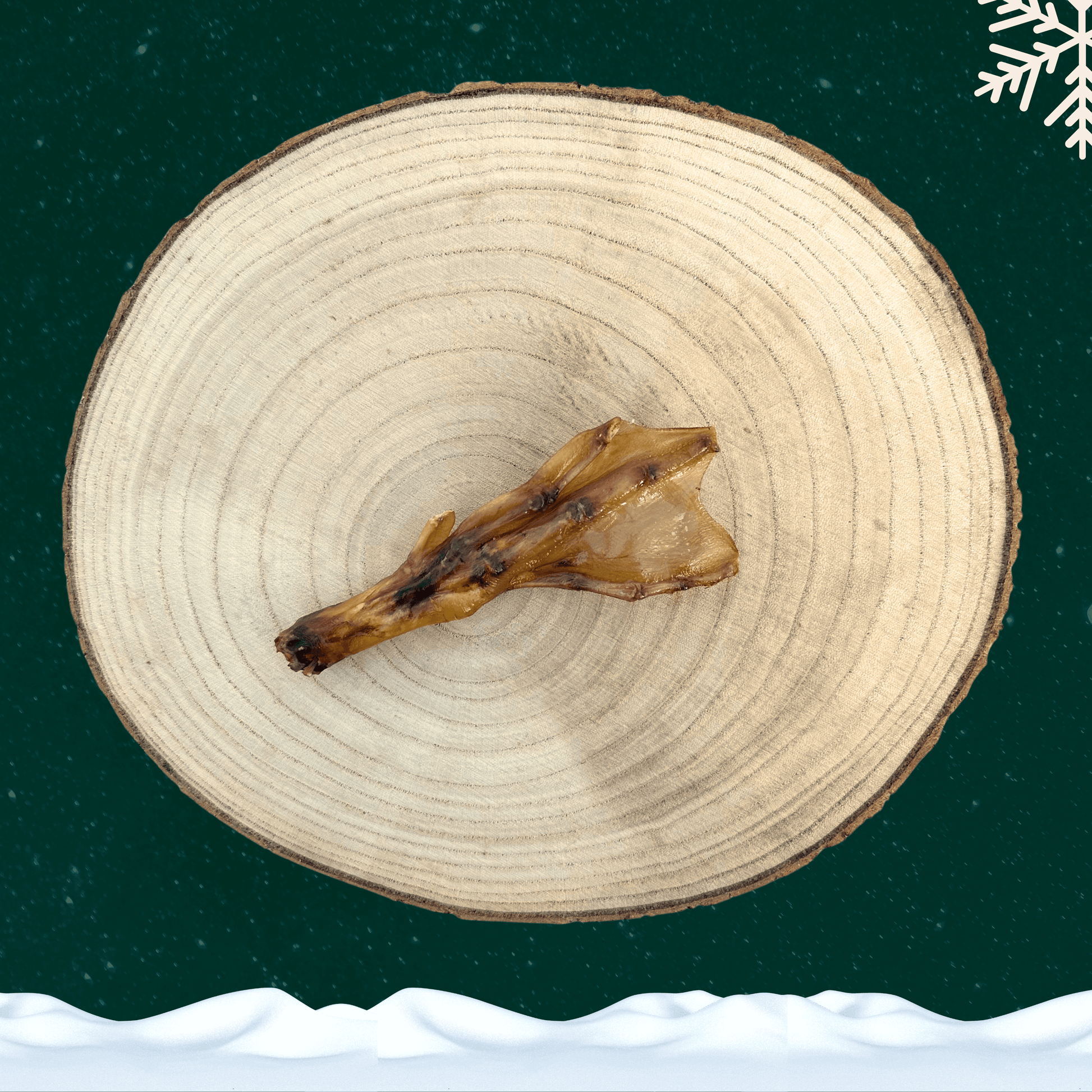 A single duck foot dog treat on wooden plate in front of a green starry sky backdrop with a white snowflake in the top right corner and a blanket of snow across the bottom.