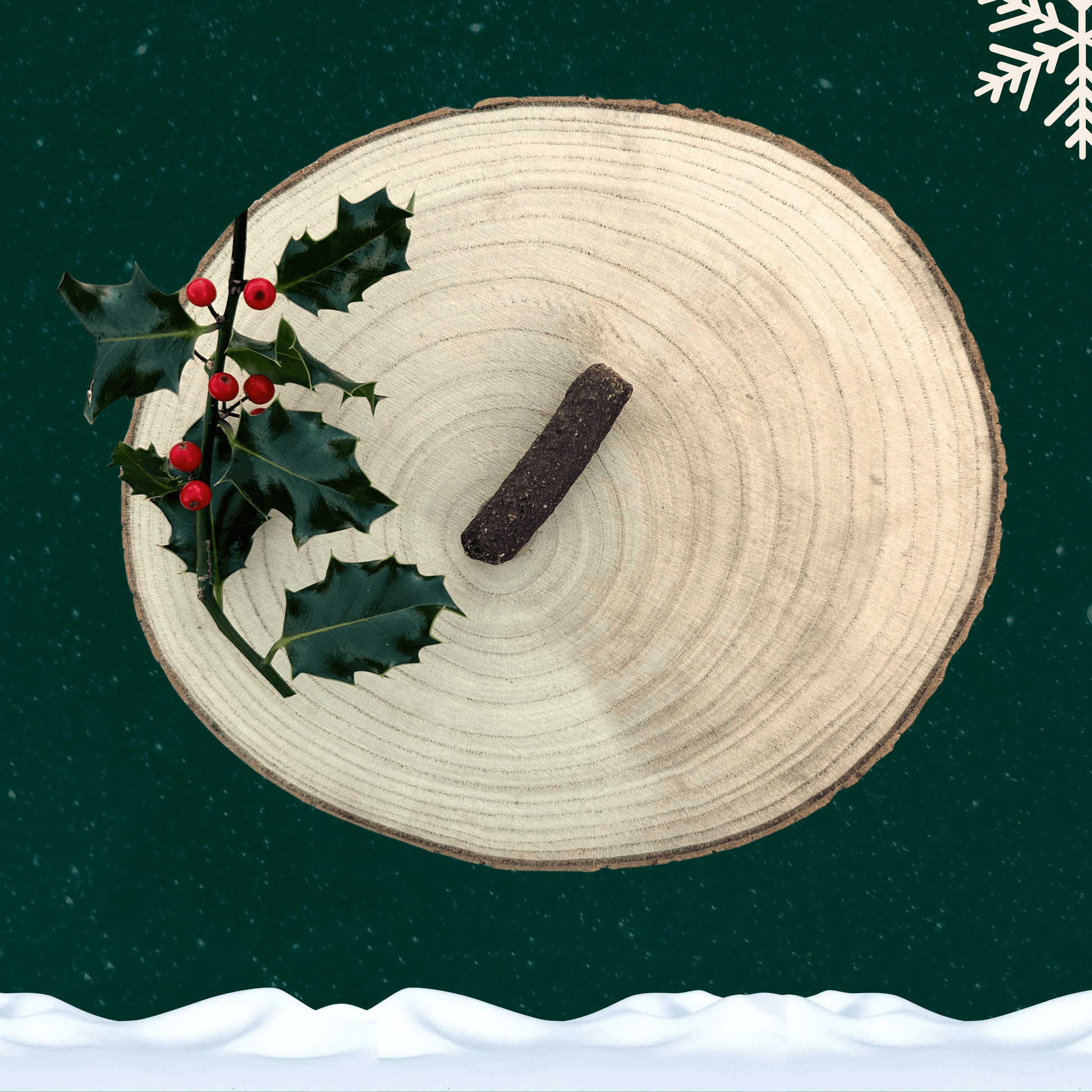 A single duck and orange cocktail sausage for dogs next to a sprig of decorative holly. All on a wooden slice plate against a dark green starry sky, with a snowflake in the top right hand corner and a blanket of snow across the bottom.