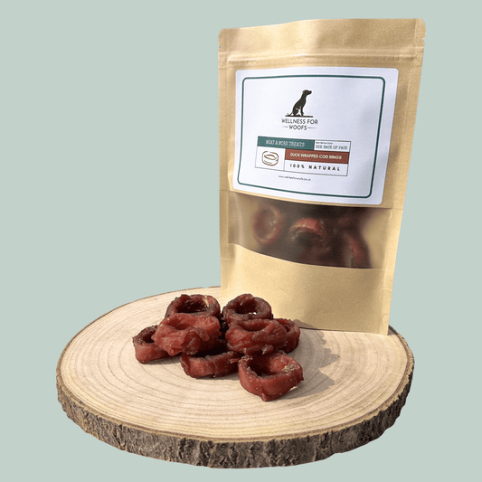 Dried cod and duck dog treats on a wooden board with a branded packaging bag on a light green background