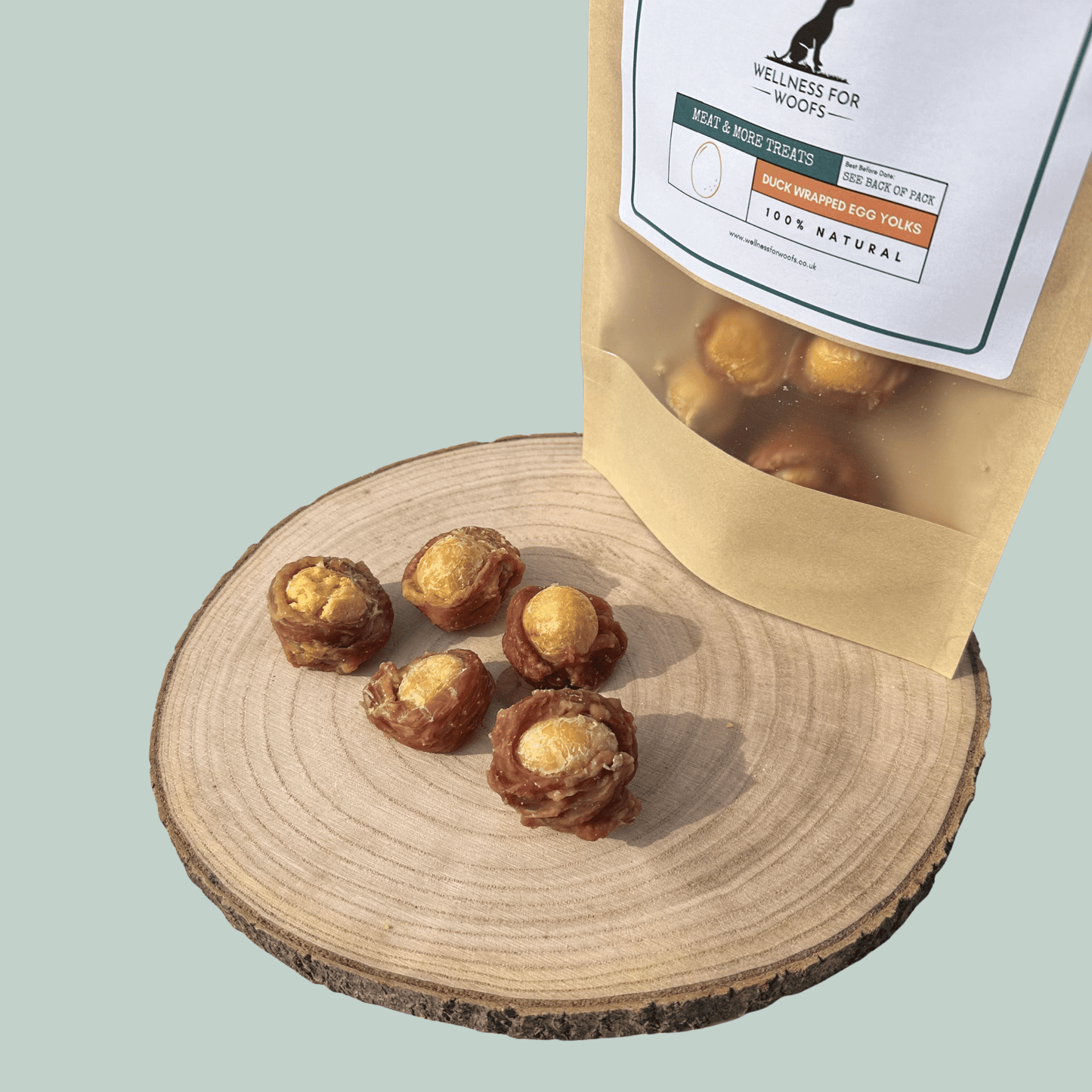 Egg yolks wrapped in dried duck on a wooden plate in front of a light green background