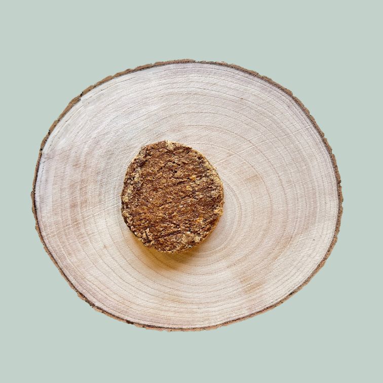 A premium quarter pounder beef burger for dogs on a wooden plate and jade green background