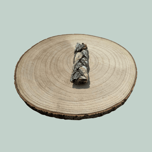 Side view of a single natural cod skin braid dog chew on a wooden slice plate against a jade green background