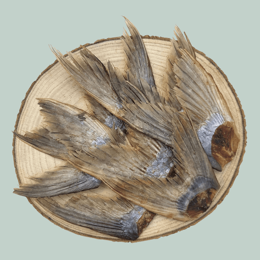 Pile of dried catfish tail natural and healthy dog treats on a wooden slice plate against a jade green background