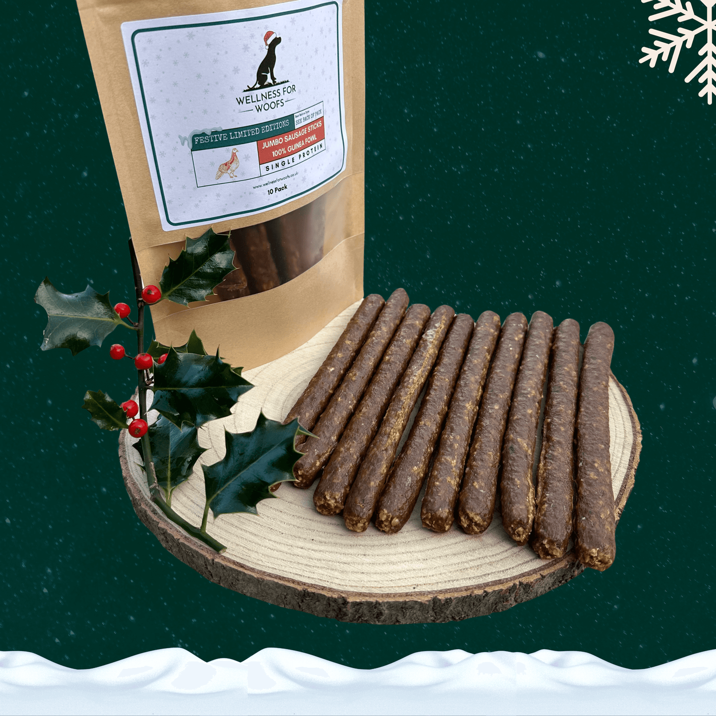 Pack of 10 guinea fowl sausage dog treats next to 10 loose sausages on a wooden plate with a piece of festive holly. All against a green starry background with a snowflake in the top right corner and snow across the bottom.