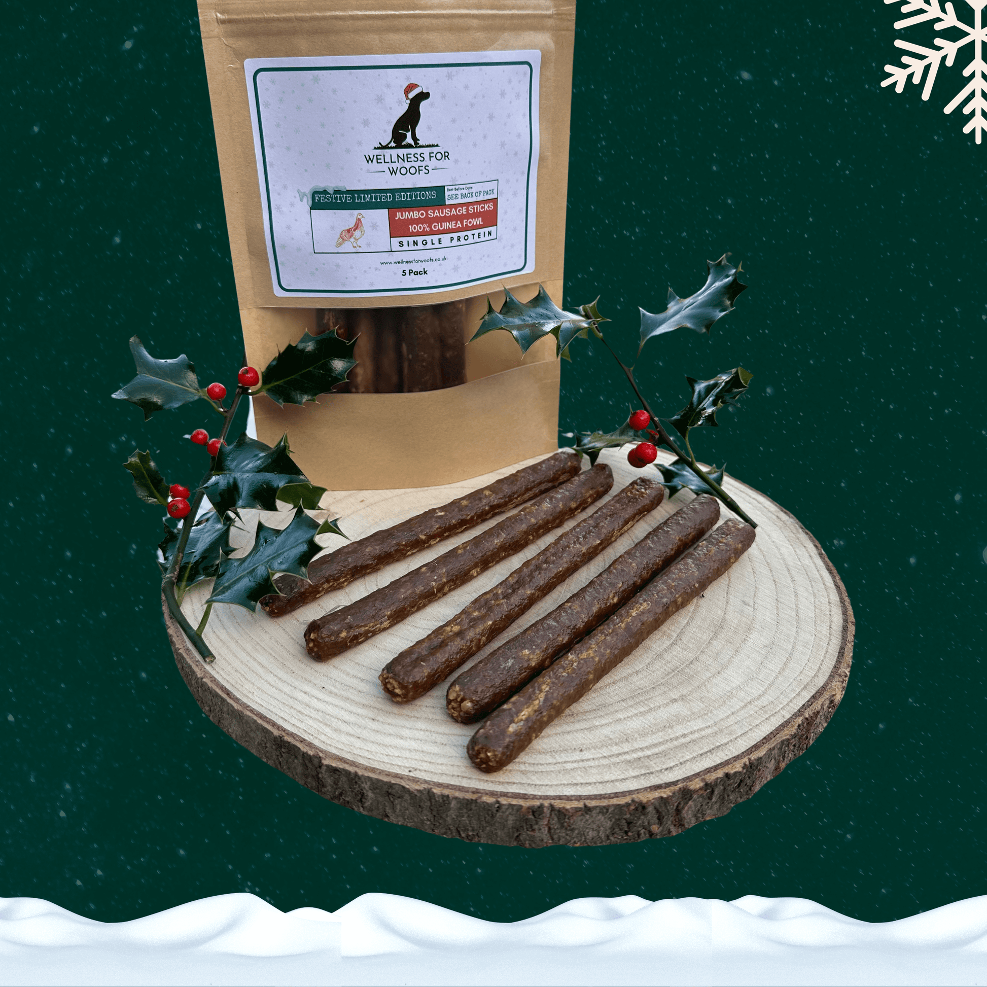 Pack of 5 guinea fowl sausage dog treats next to 5 loose sausages on a wooden plate with a piece of festive holly. All against a green starry background with a snowflake in the top right corner and snow across the bottom.