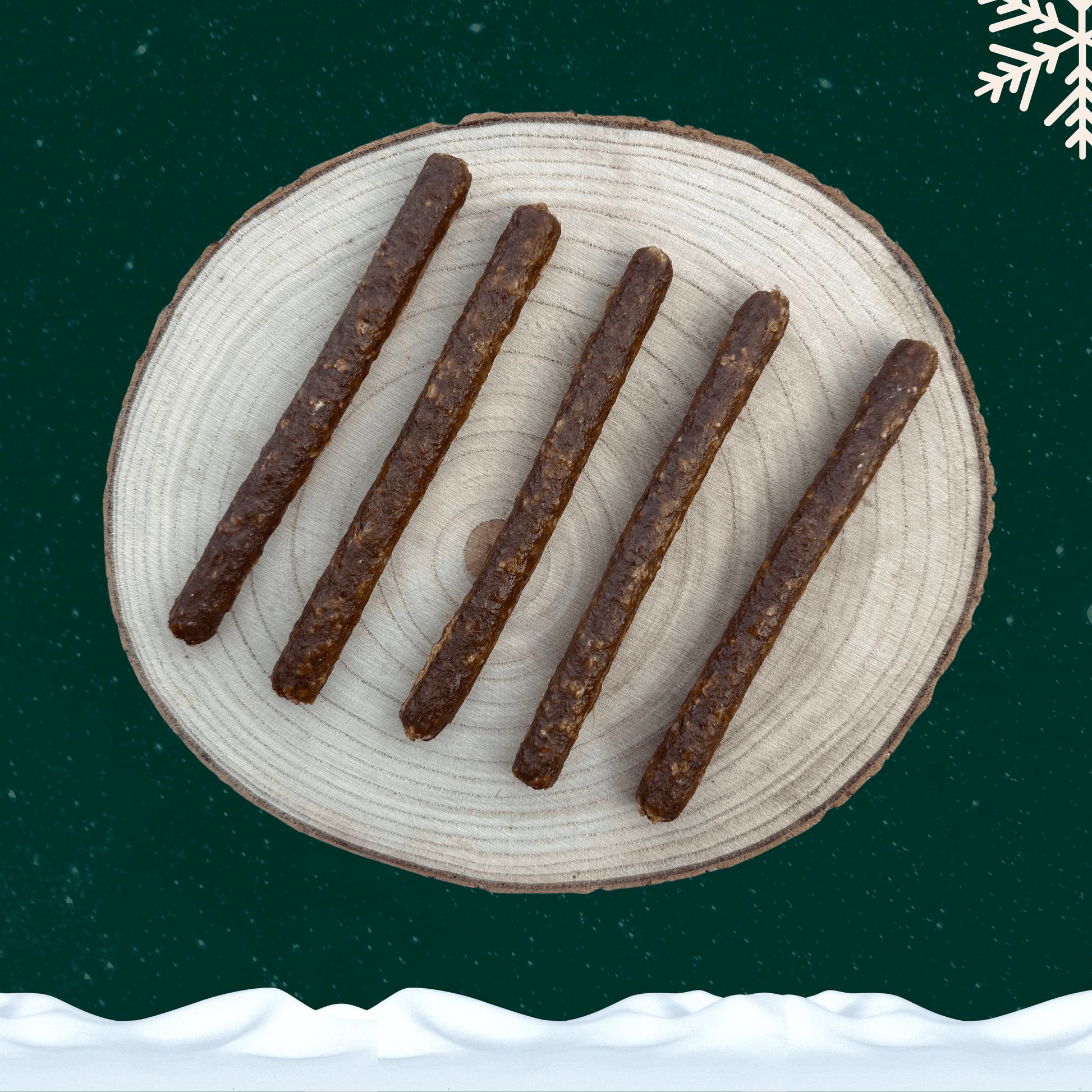 5 guinea fowl sausage sticks for dogs lay neatly on a wooden plate against a starry green background, a snowflake in the top right corner and snow across the bottom.