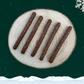 5 guinea fowl sausage sticks for dogs lay neatly on a wooden plate against a starry green background, a snowflake in the top right corner and snow across the bottom.