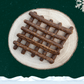 10 guinea fowl sausage sticks for dogs piled neatly on a wooden plate against a starry green background, a snowflake in the top right corner and snow across the bottom.