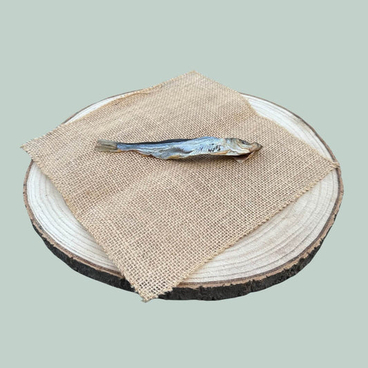 Individual dried herring dog treat lay on a wooden plate and jade green background