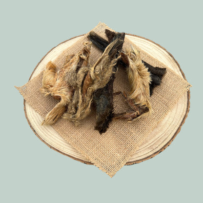 Pieces of dried furry lamb skin natural dog chews on a wooden plate and jade green background.