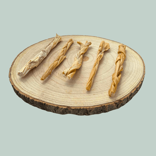 Side view of 5 braided lamb skin chews for dogs on a wood slice plate against a jade green background